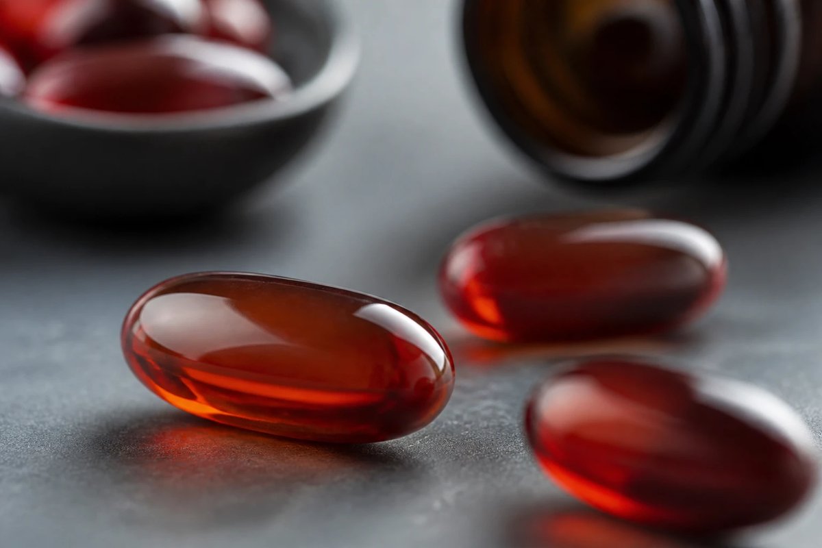 Makroaufnahme durchscheinender Weichkapseln, gefüllt mit tiefrot-orangem Astaxanthin-Öl, auf einer kühlen neutralen Oberfläche