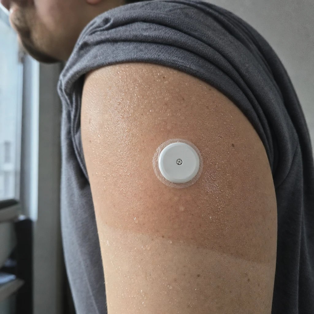 Nahaufnahme eines kleinen runden weißen Glukosesensors auf der verschwitzten Rückseite des Oberarms eines Athleten nach einer harten Einheit
