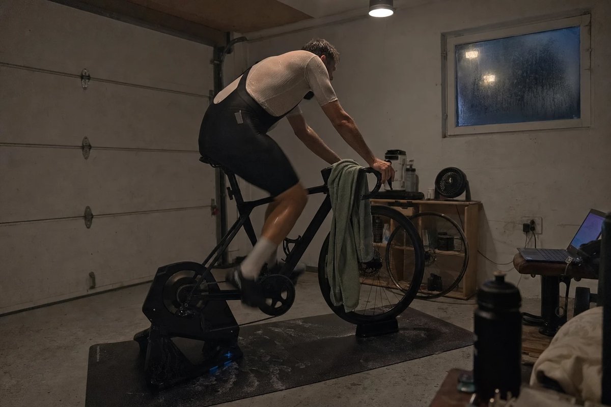 Rennrad auf dem Smarttrainer in einer geschlossenen Garage ohne Ventilator, Sportler beim Hitzetraining mit Schweiß auf der Matte
