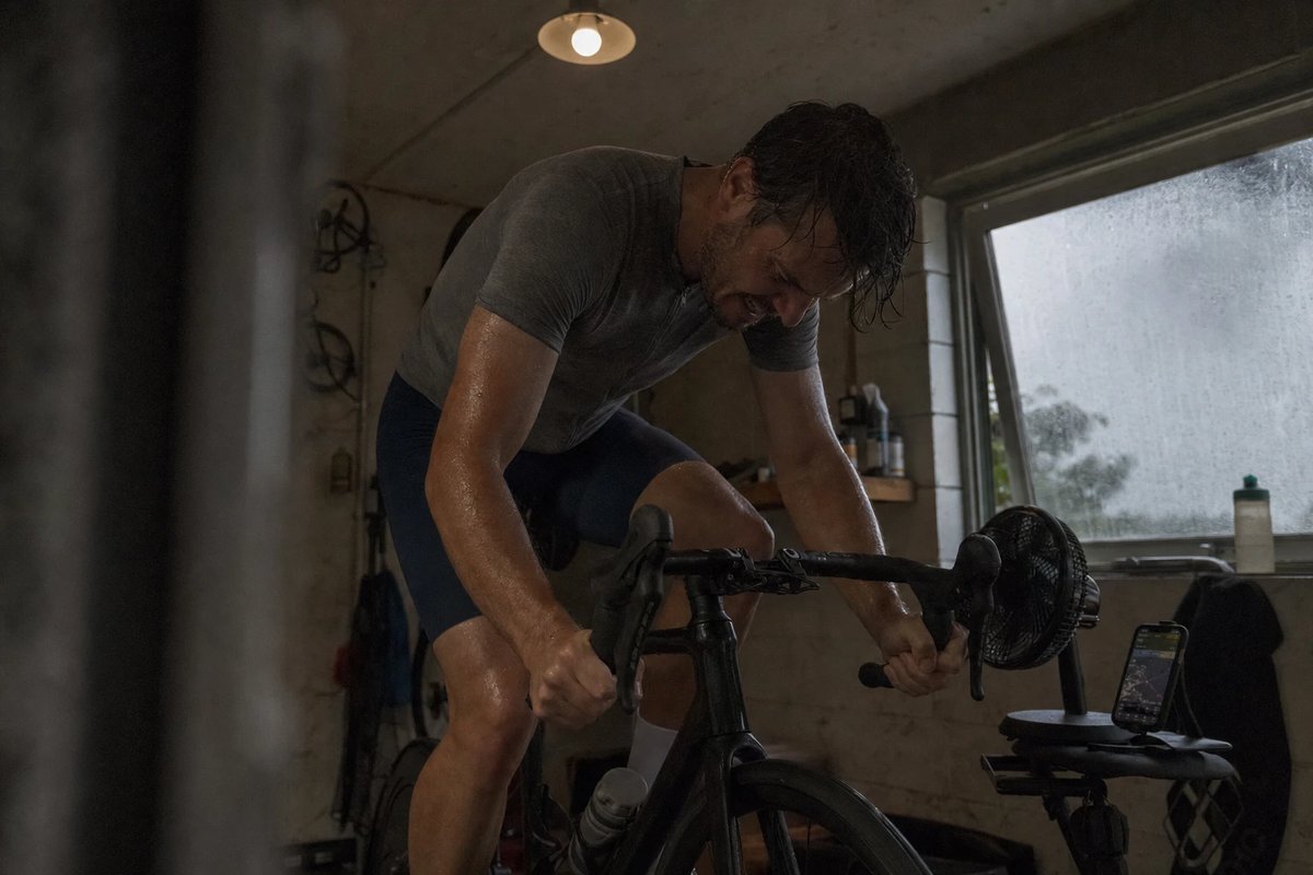 Radfahrer auf einem Smarttrainer in einer kleinen Garage, Kopf gesenkt und Kiefer angespannt in voller Konzentration während einer harten Einheit