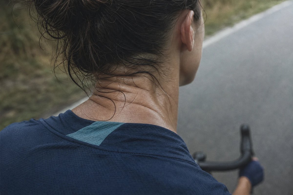 Nacken und obere Schultern einer Radfahrerin von hinten und leicht oben fotografiert, der Kopf nach hinten gestreckt um nach vorne zu schauen, gespannte Sehnen am unteren Nacken und angespannter oberer Trapez sichtbar