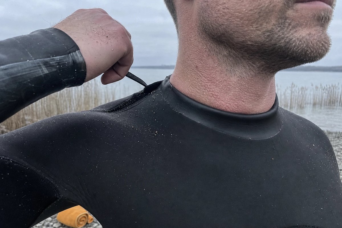 Nahaufnahme eines Schwimmers am Seeufer, der den engen Neoprenkragen seines Anzugs schließt, der Kragen drückt sichtbar in den Hals
