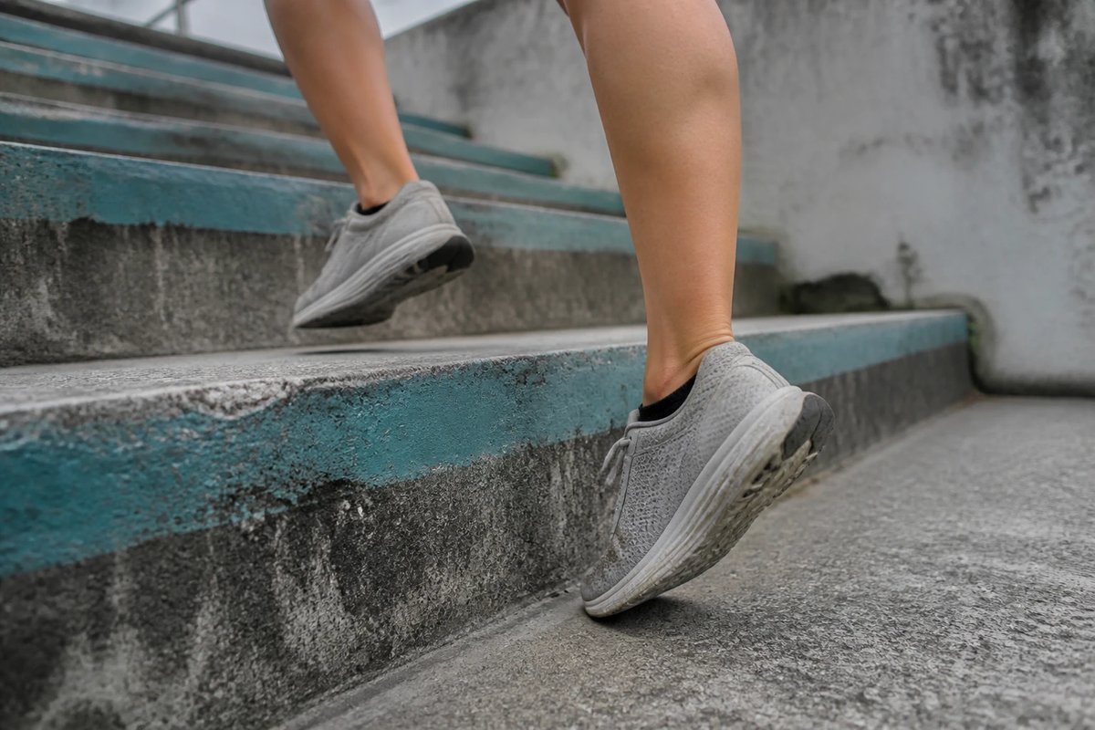 Nahaufnahme der Unterschenkel und Füße einer Läuferin auf einer steilen Betontreppe, ein Vorfuß drückt auf der Stufenkante ab, während das andere Bein zur nächsten Stufe zieht