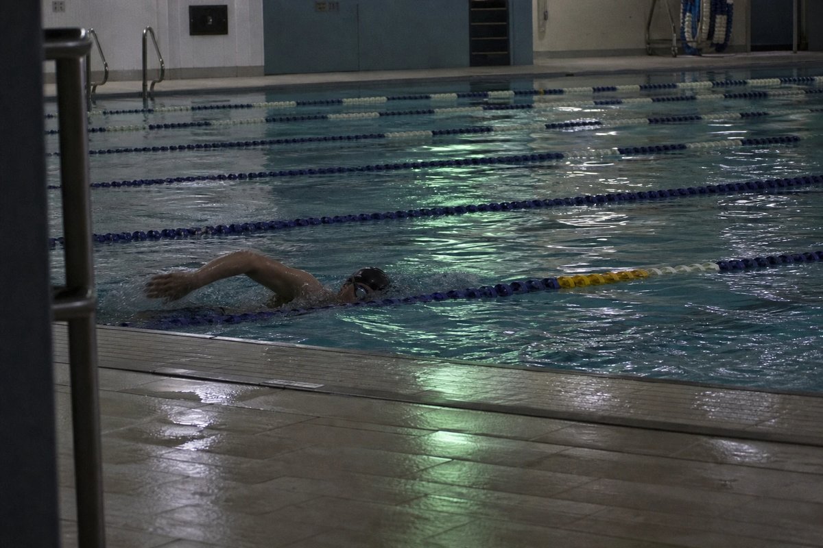 Einzelner Schwimmer zieht früh morgens seine Bahnen in einem leeren Hallenbad bei grünlichem Kunstlicht