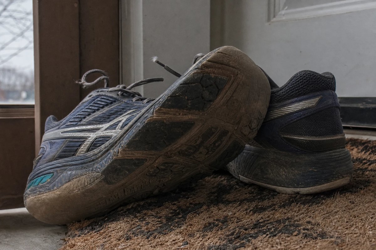 Paar abgenutzter Laufschuhe auf einer Fußmatte, die Außensohle zeigt das stärkste Verschleißmuster an der äußeren Ferse, typisch für einen Fersenaufsatz
