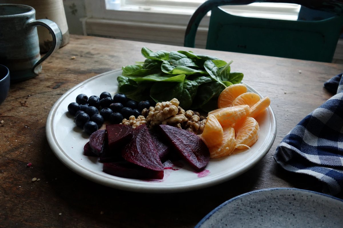 Teller mit antioxidantienreichen Lebensmitteln auf einem Holztisch: dunkle Beeren, geschnittene rote Bete, Blattgemüse, Walnüsse und Orangenstücke
