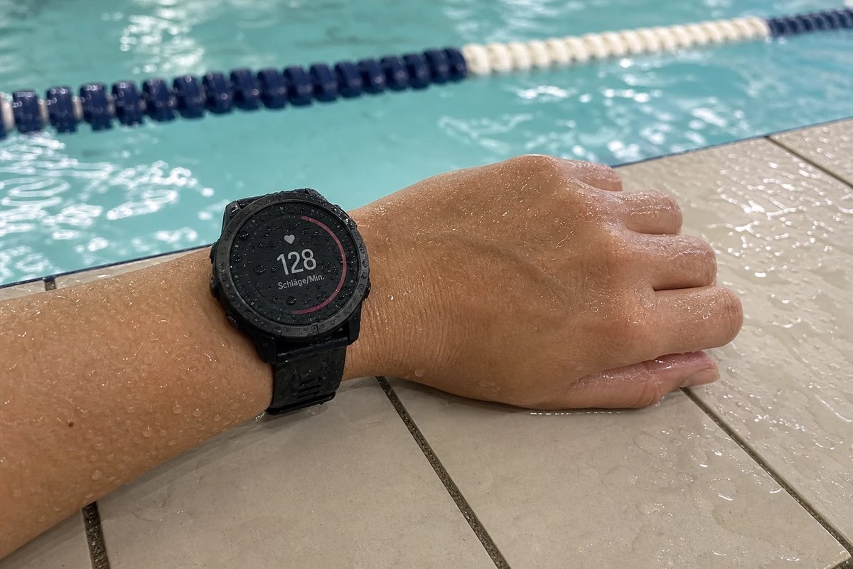 Wasserdichte Sportuhr am Handgelenk auf dem nassen Beckenrand zeigt nach einer Aqua-Jogging-Einheit den Wert 128 bpm