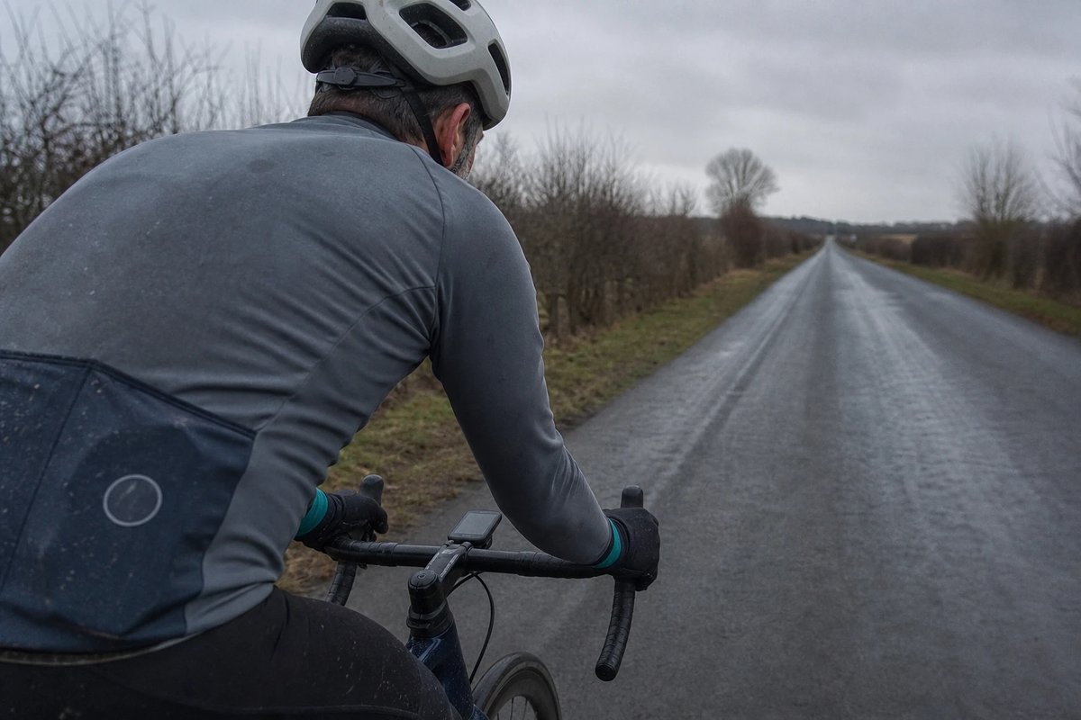 Radfahrer auf einer lockeren winterlichen Grundlagen-Ausfahrt auf einer ruhigen, nassen Landstraße, von hinten über die Schulter aufgenommen