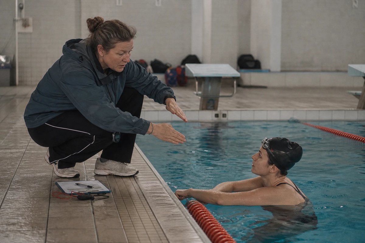 Schwimmtrainerin am Beckenrand gibt einer Schwimmerin am Beckenrand mit der Hand ein Zeichen für einen schmaleren Beinschlag