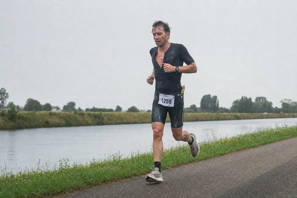 Einzelner Triathlet läuft spät im Rennen erschöpft auf einem flachen Weg am Kanal entlang