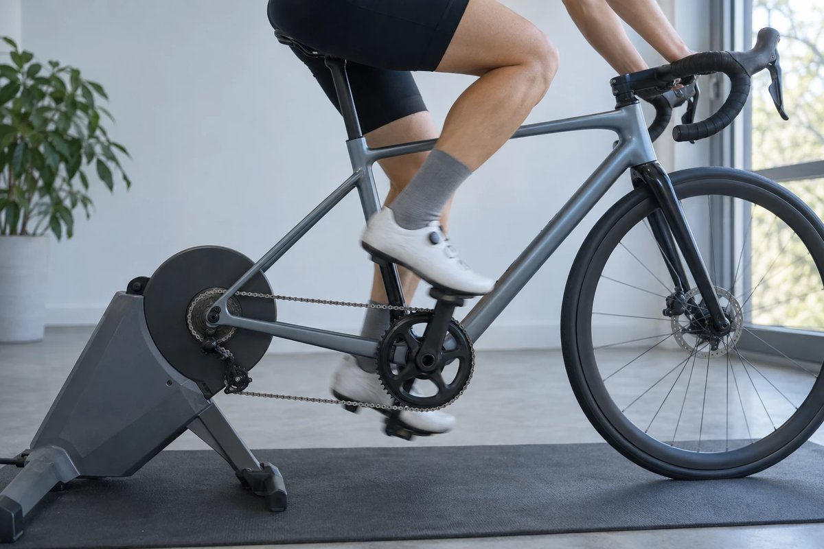 Radfahrerin auf einem Rennrad im Rollentrainer, von der Antriebsseite fotografiert, ein Bein mit gebeugtem Knie am oberen Punkt der Pedalumdrehung