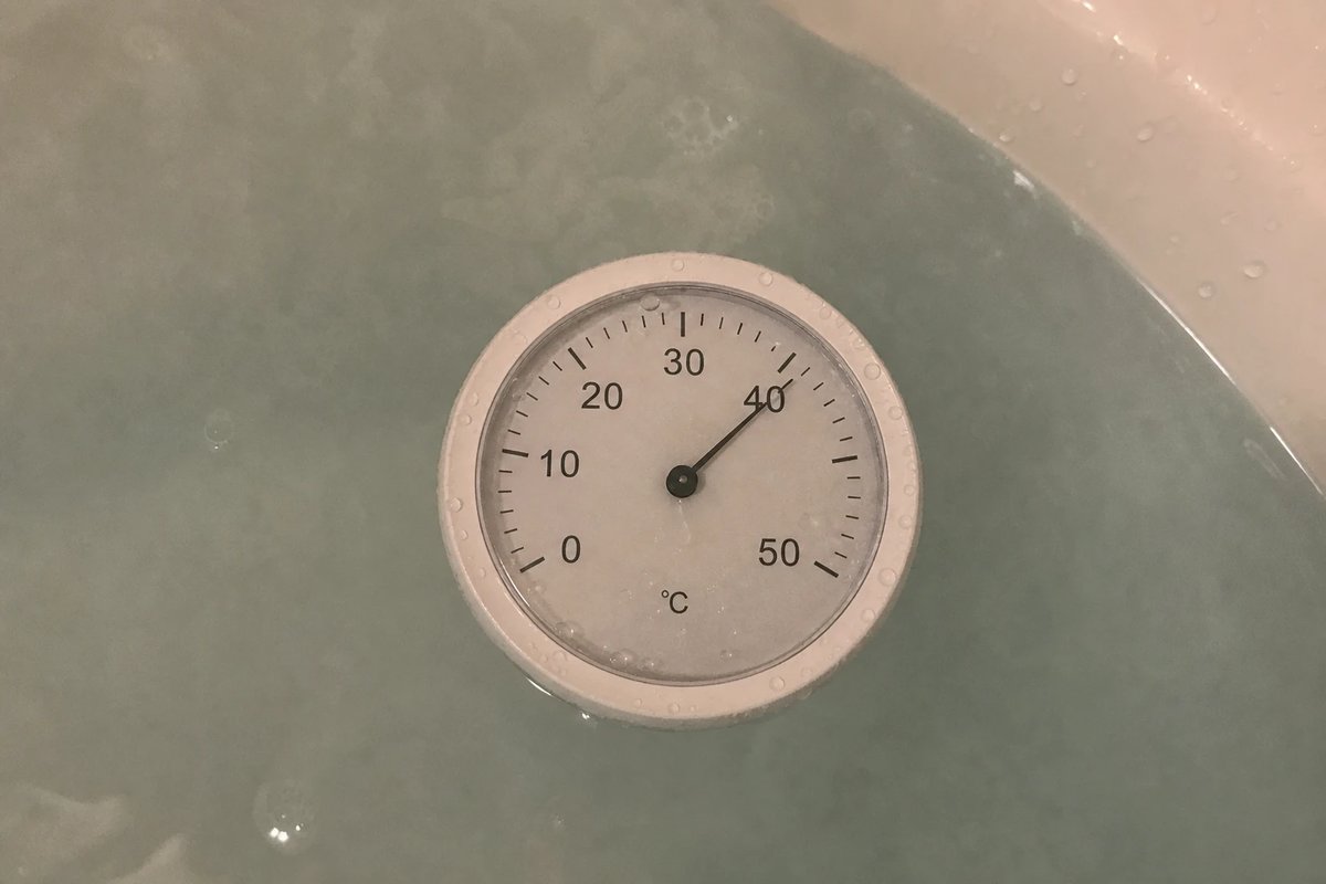 Schwimmendes Badethermometer auf dampfendem Badewasser von oben abgelesen, die Nadel zeigt auf 40 Grad Celsius