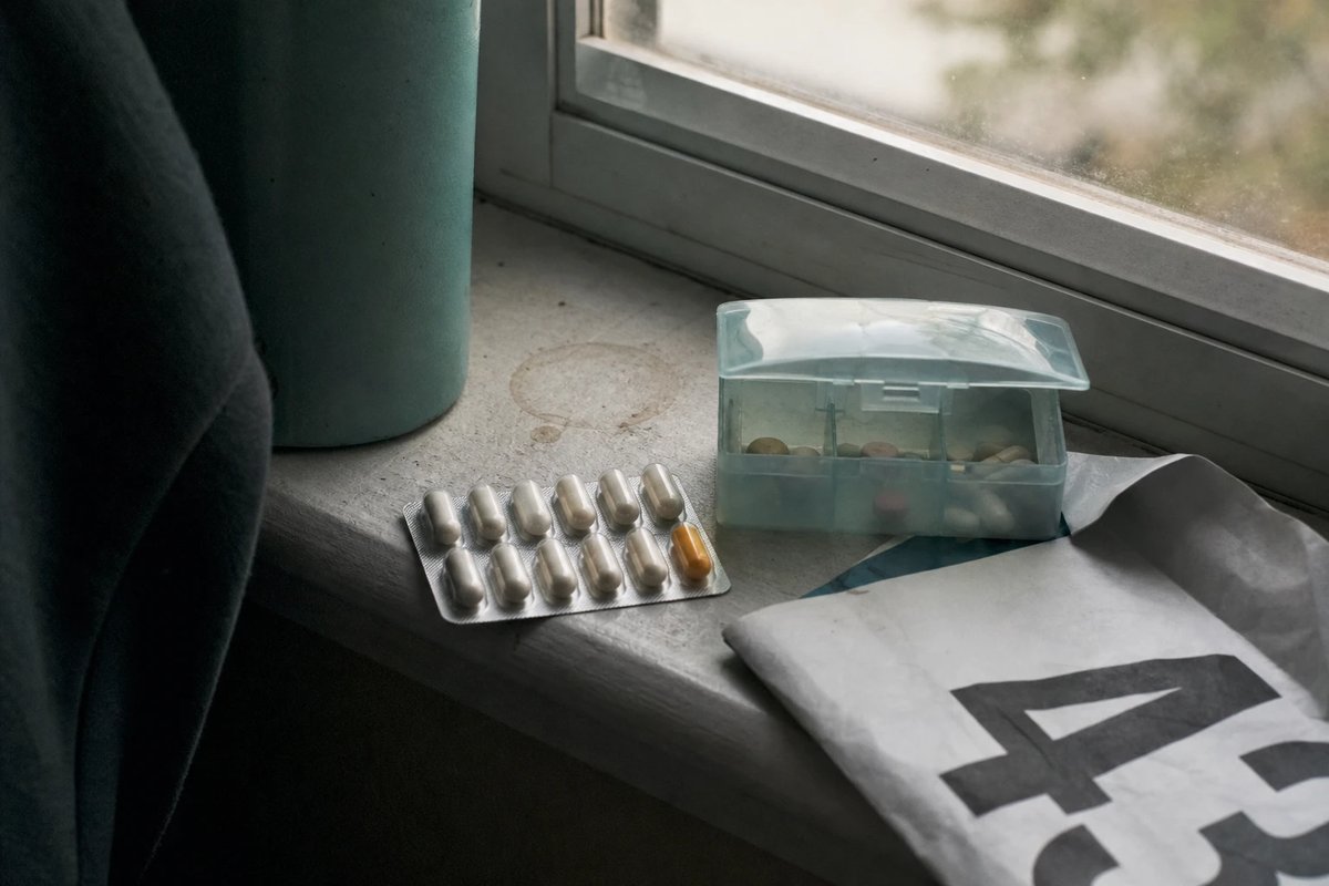 Blisterstreifen mit Probiotika-Kapseln, eine kleine Tagesbox und eine Trinkflasche neben einer Startnummer auf einer Fensterbank im Morgenlicht