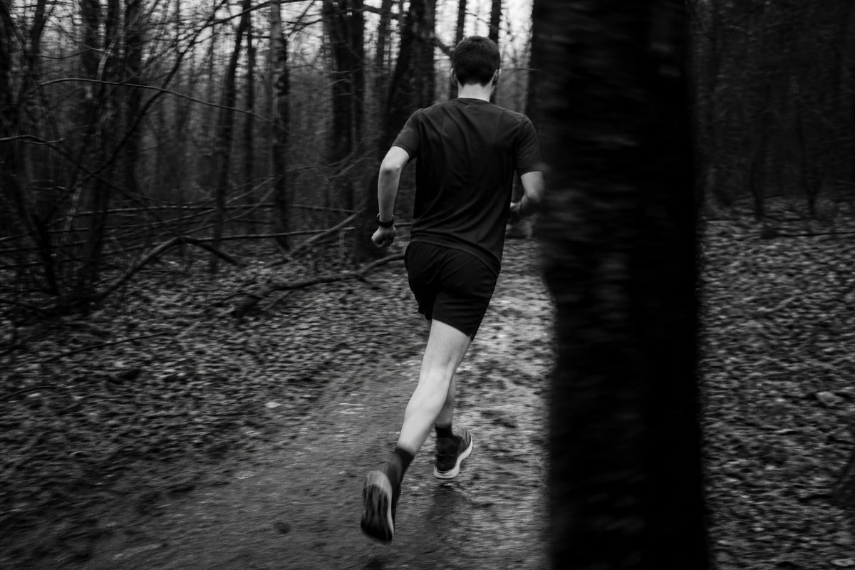 Läufer von hinten auf einem nassen Waldweg mit aufrechtem, stabilem Oberkörper und ruhiger Beckenhaltung mitten im Schritt