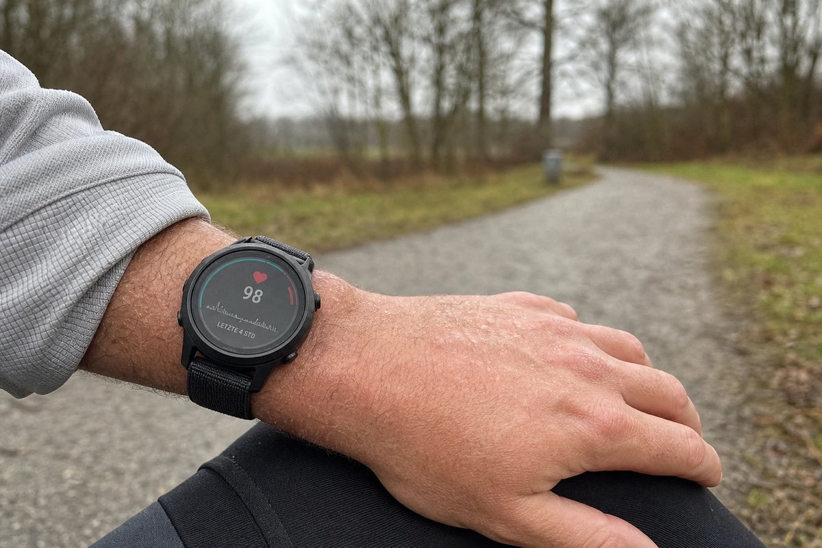 Sportuhr am Handgelenk zeigt einen niedrigen Puls von 98 bpm bei einer ersten lockeren Einheit nach der Krankheit auf einem grauen Parkweg