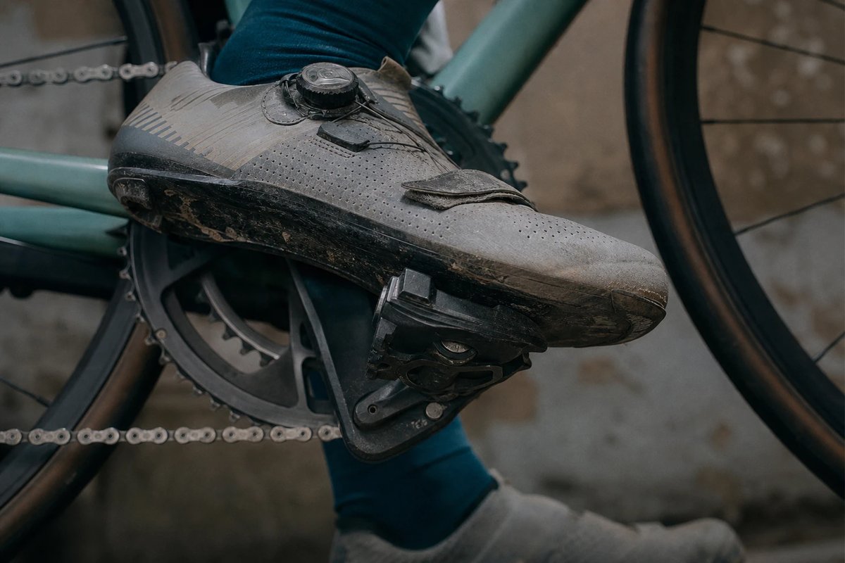 Seitenansicht eines abgenutzten Rennradschuhs mit Carbonsohle, in das Klickpedal eingeklickt an der Kurbel, Fokus auf Cleat und Vorfuß, leicht geöffneter Boa-Verschluss