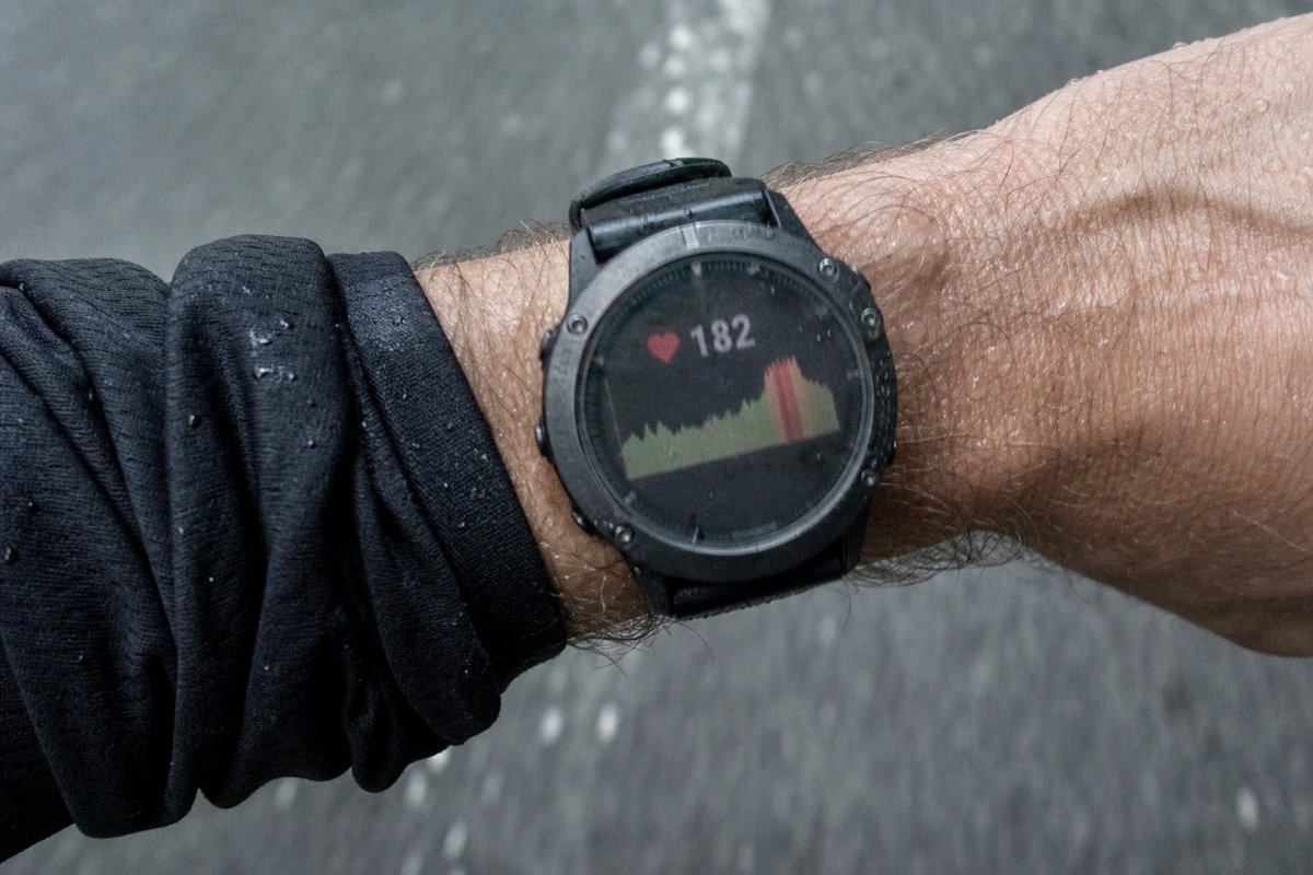 Nahaufnahme eines verschwitzten Handgelenks mit einer Sport-GPS-Uhr, die während einer harten Einheit eine hohe Herzfrequenz und einen Pulsverlauf anzeigt